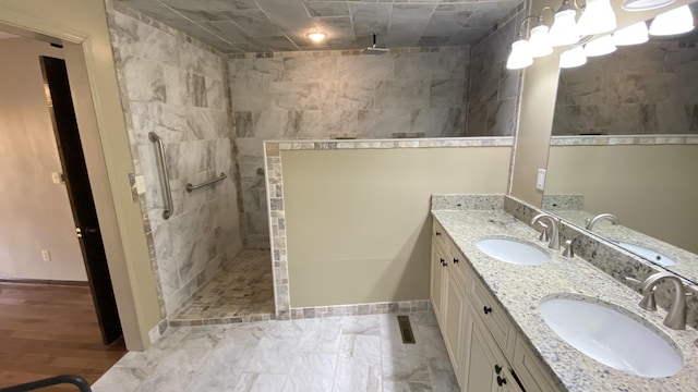 bathroom with a walk in shower, double vanity, a sink, and baseboards