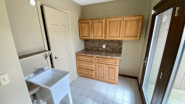 kitchen featuring a sink, light tile patterned floors, baseboards, and backsplash