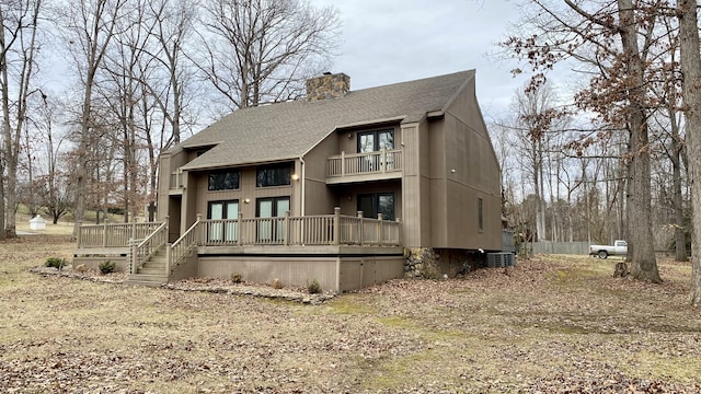 back of property with a deck, roof with shingles, a chimney, and a balcony