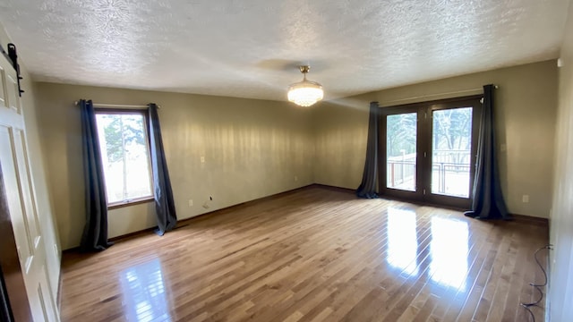 unfurnished room with a textured ceiling, french doors, a barn door, and light wood-style flooring