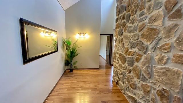 hall featuring light wood-type flooring, a towering ceiling, and baseboards