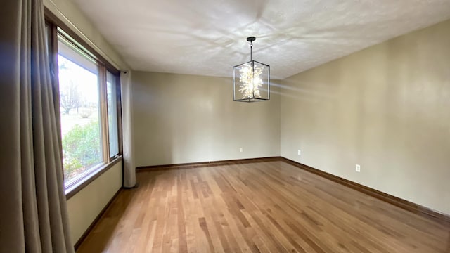 spare room with a chandelier, light wood-type flooring, and baseboards