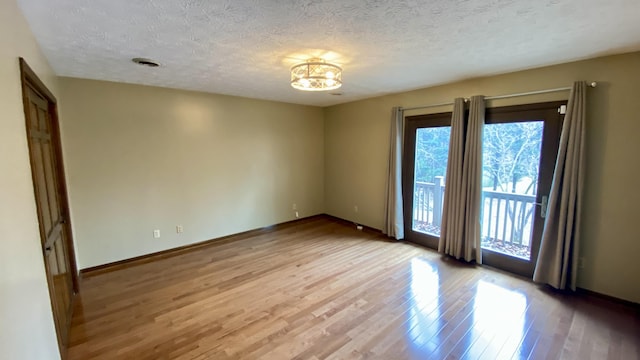 empty room featuring a textured ceiling, light wood finished floors, and baseboards