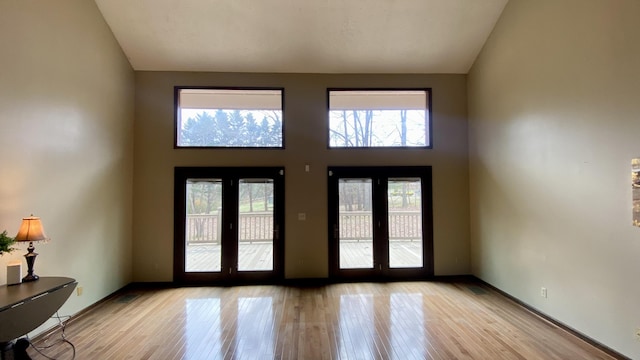 entryway with light wood-type flooring, a high ceiling, baseboards, and french doors