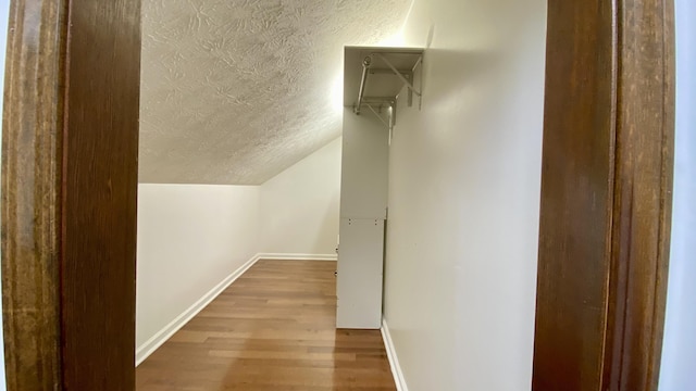 bonus room featuring light wood-style floors, baseboards, vaulted ceiling, and a textured ceiling