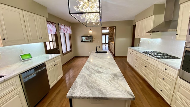 kitchen with decorative light fixtures, appliances with stainless steel finishes, a kitchen island, light stone countertops, and wall chimney exhaust hood