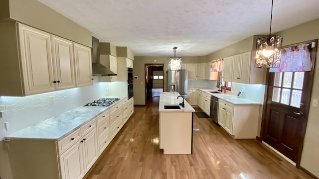 kitchen featuring wall chimney exhaust hood, light countertops, a sink, and decorative light fixtures