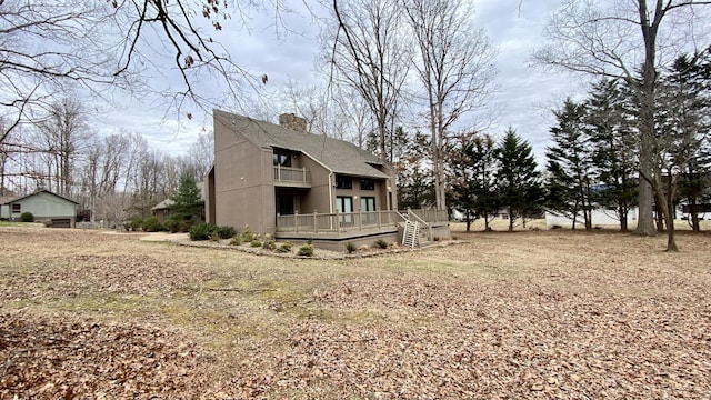 rear view of property featuring a balcony, a chimney, and a wooden deck