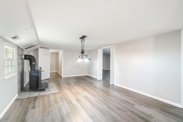 unfurnished living room with light wood-type flooring, a wood stove, a textured ceiling, and vaulted ceiling