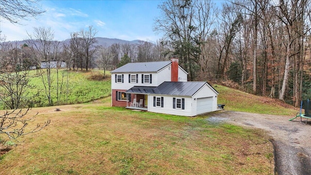 view of front of home with covered porch, a trampoline, a garage, a mountain view, and a front lawn