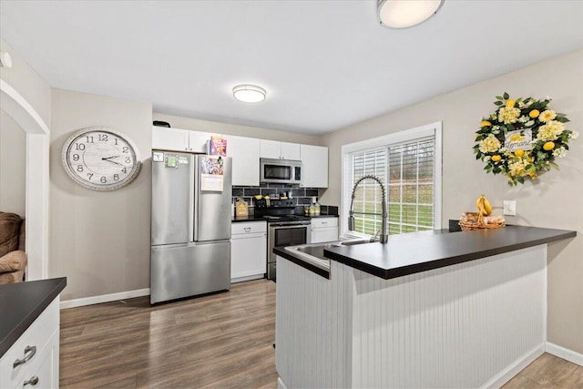 kitchen with dark wood-type flooring, backsplash, stainless steel appliances, white cabinets, and kitchen peninsula