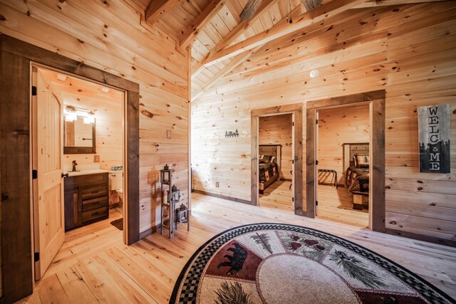 hallway with lofted ceiling with beams, sink, wooden walls, light wood-type flooring, and wood ceiling