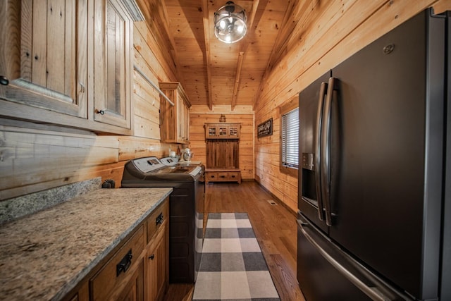 kitchen featuring light stone counters, independent washer and dryer, stainless steel fridge, wood walls, and vaulted ceiling