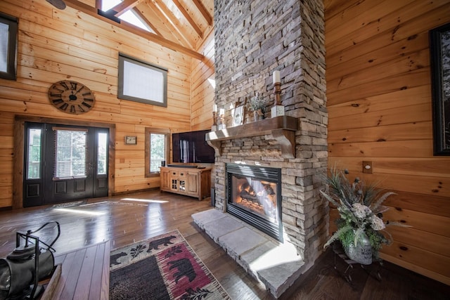 unfurnished living room with dark hardwood / wood-style floors, high vaulted ceiling, wooden walls, and a stone fireplace