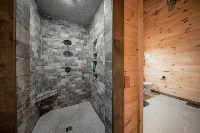 bathroom with toilet, a tile shower, and wooden walls