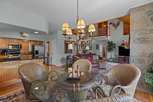 dining room with baseboards, a towering ceiling, light wood-style flooring, and a notable chandelier