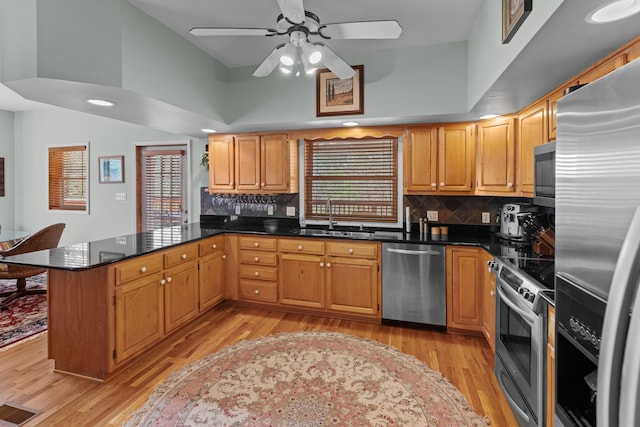 kitchen with a sink, appliances with stainless steel finishes, a peninsula, visible vents, and light wood-style floors