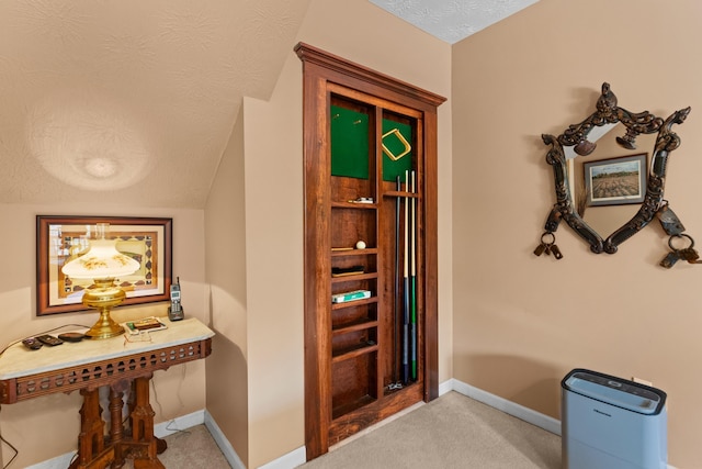 corridor with light colored carpet, baseboards, and a textured ceiling