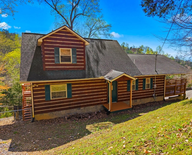 cabin featuring a front yard, a shingled roof, and a deck
