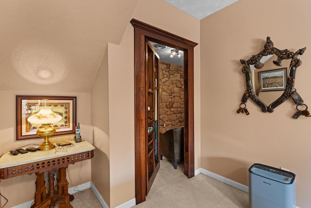 corridor with light colored carpet, lofted ceiling, baseboards, and a textured ceiling