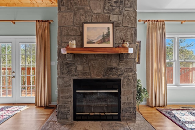 interior details with french doors, baseboards, visible vents, a stone fireplace, and wood finished floors