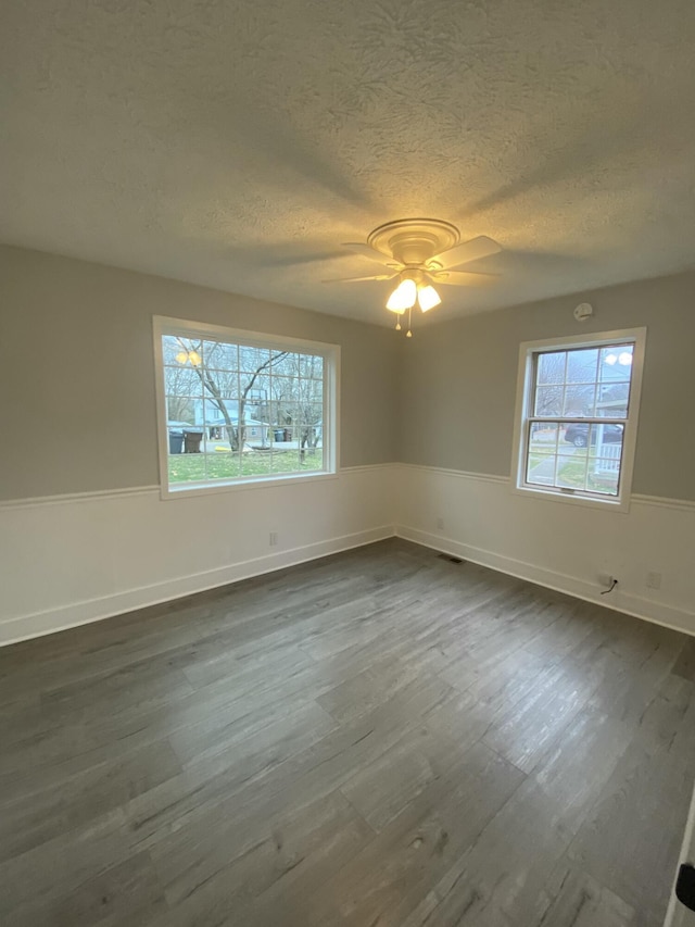 unfurnished room with a textured ceiling, ceiling fan, dark hardwood / wood-style floors, and a wealth of natural light