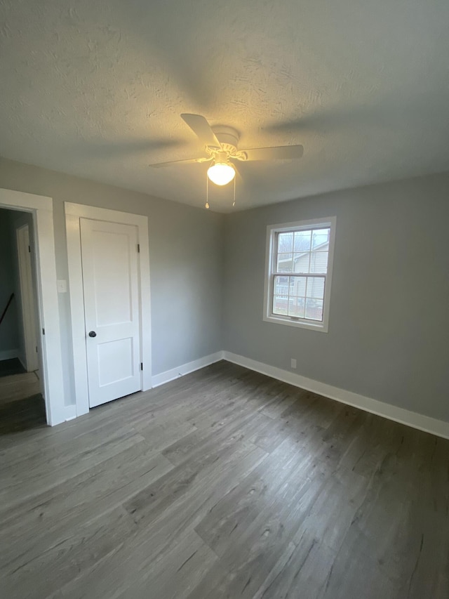 unfurnished bedroom with ceiling fan, a closet, wood-type flooring, and a textured ceiling