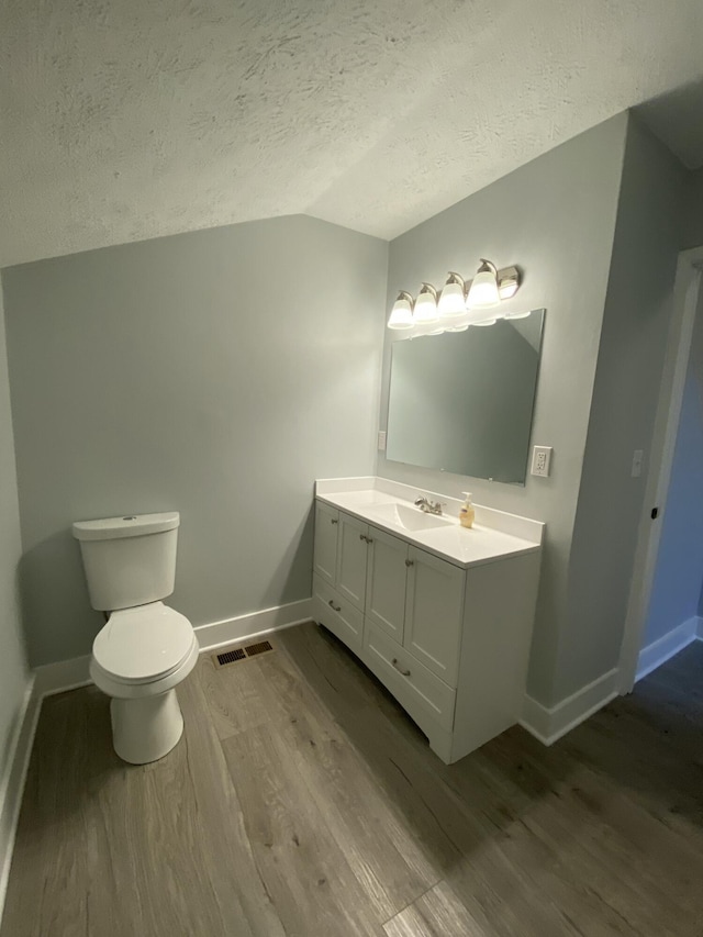 bathroom with vaulted ceiling, wood-type flooring, vanity, a textured ceiling, and toilet