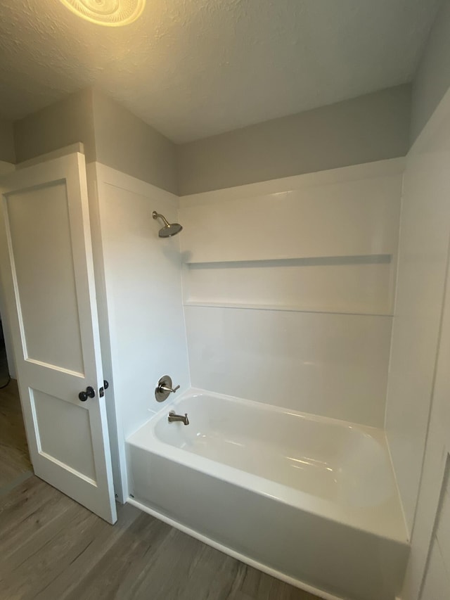 bathroom with a textured ceiling, shower / bathtub combination, and wood-type flooring