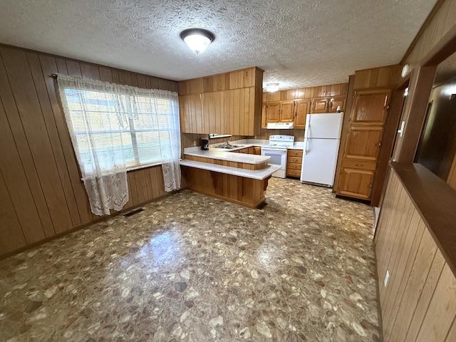 kitchen featuring a textured ceiling, kitchen peninsula, wood walls, and white appliances