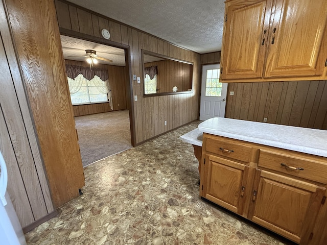 kitchen with wooden walls, ceiling fan, light colored carpet, and a textured ceiling