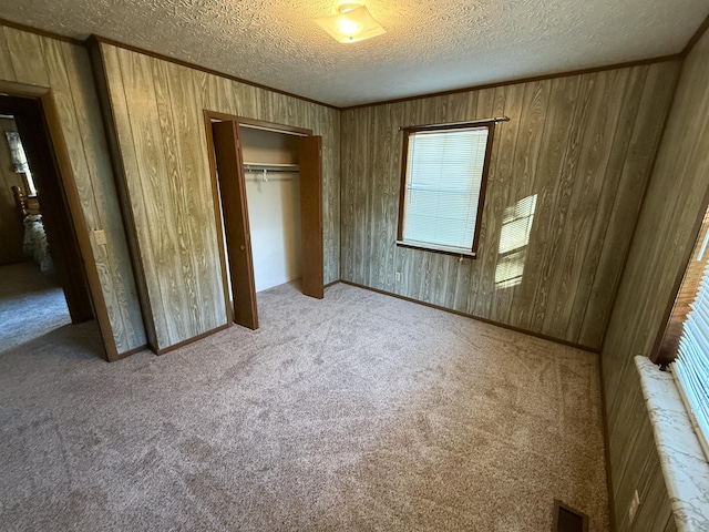 unfurnished bedroom with light carpet, a textured ceiling, a closet, and wooden walls