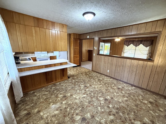 kitchen with sink, white range, kitchen peninsula, wood walls, and a textured ceiling