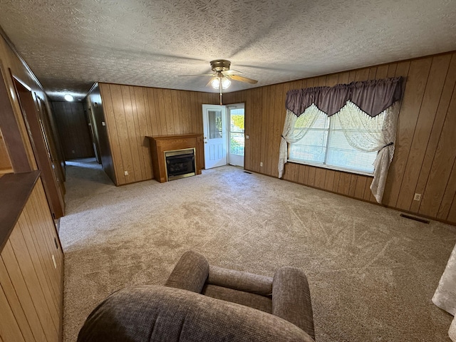 carpeted living room featuring ceiling fan, a textured ceiling, and wooden walls