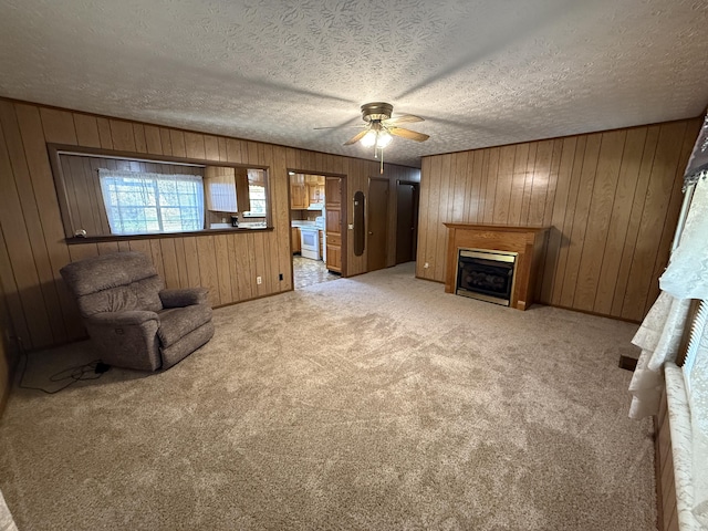 unfurnished room featuring a textured ceiling, light colored carpet, ceiling fan, and wooden walls