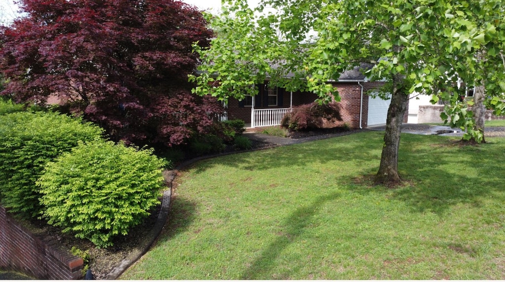 view of yard with a porch, driveway, and an attached garage