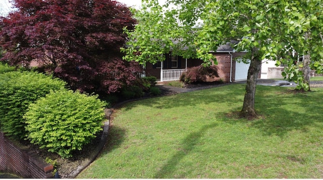view of yard with a porch, driveway, and an attached garage