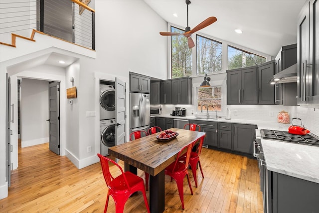 kitchen featuring tasteful backsplash, stacked washer / dryer, extractor fan, stainless steel appliances, and a sink