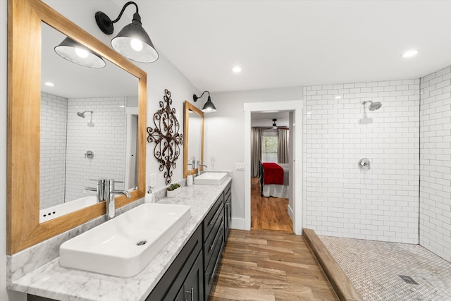 ensuite bathroom featuring a tile shower, double vanity, and a sink