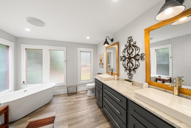 bathroom with toilet, wood finished floors, a sink, a freestanding bath, and double vanity