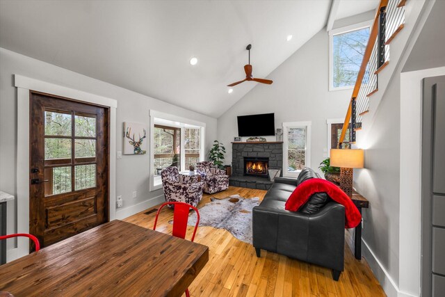 living room with light wood finished floors, baseboards, stairs, a fireplace, and high vaulted ceiling