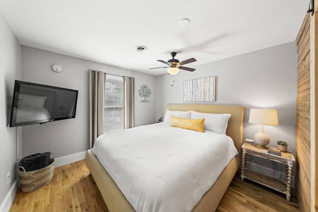 bedroom featuring ceiling fan, wood finished floors, visible vents, and baseboards