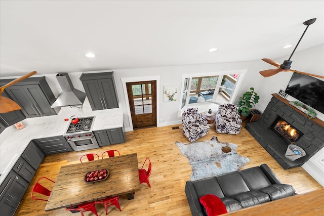 living area featuring a warm lit fireplace, visible vents, a ceiling fan, light wood-style floors, and recessed lighting