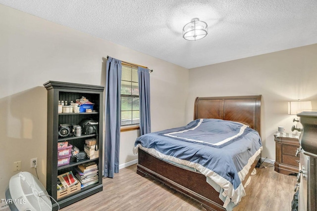 bedroom featuring light wood-type flooring, baseboards, and a textured ceiling