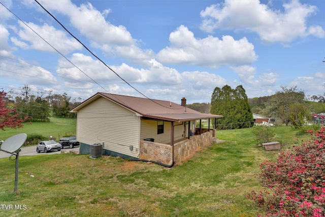view of home's exterior with central air condition unit, a lawn, a chimney, and metal roof