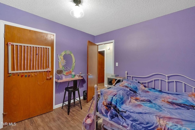 bedroom featuring baseboards, wood finished floors, and a textured ceiling