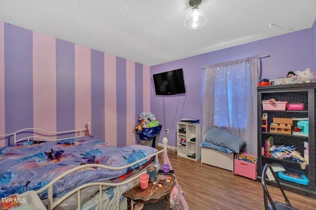 bedroom with wallpapered walls, wood finished floors, and a textured ceiling