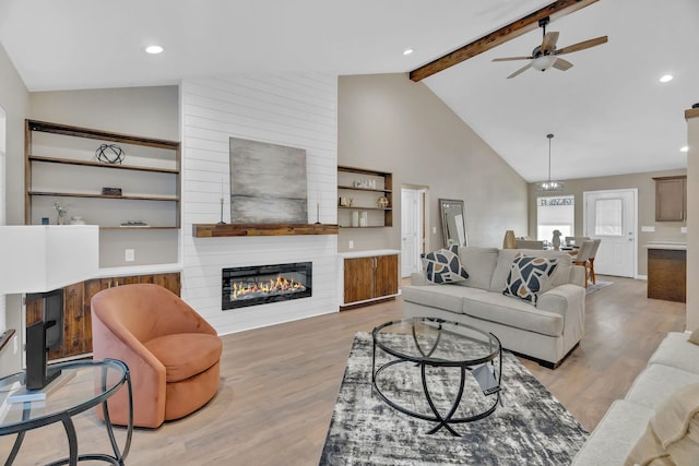 living area featuring high vaulted ceiling, light wood-style flooring, a fireplace, a ceiling fan, and beamed ceiling