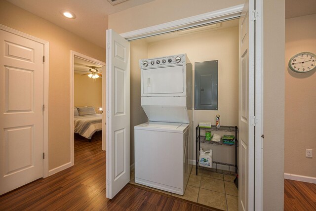 washroom featuring electric panel, laundry area, dark wood-style flooring, stacked washing maching and dryer, and baseboards