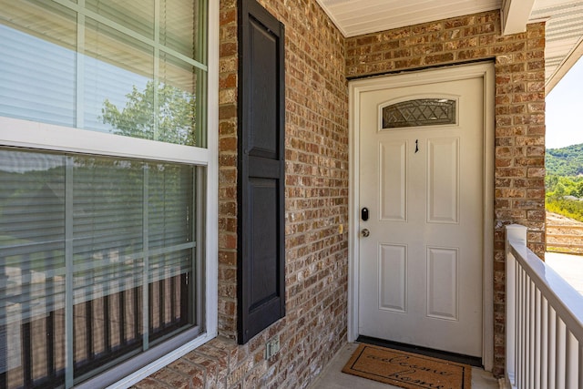 doorway to property featuring a porch and brick siding